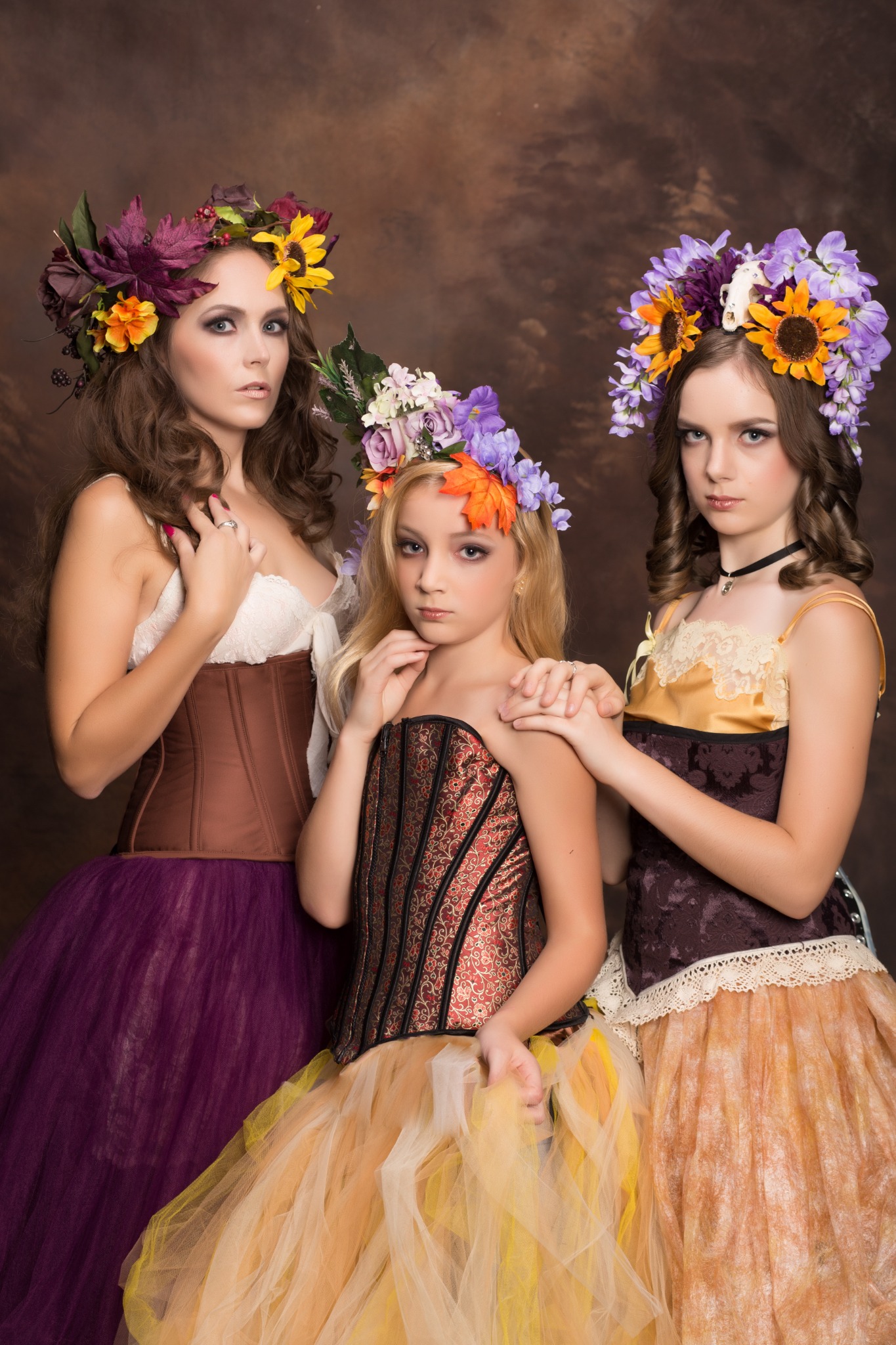 Mother and two daughters wearing colorful floral crowns in a fine-art family portrait.