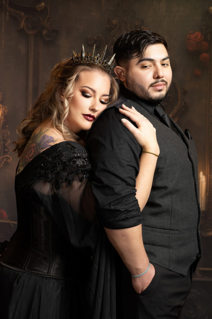 Couple dressed in black sharing a close embrace during a dramatic studio portrait.