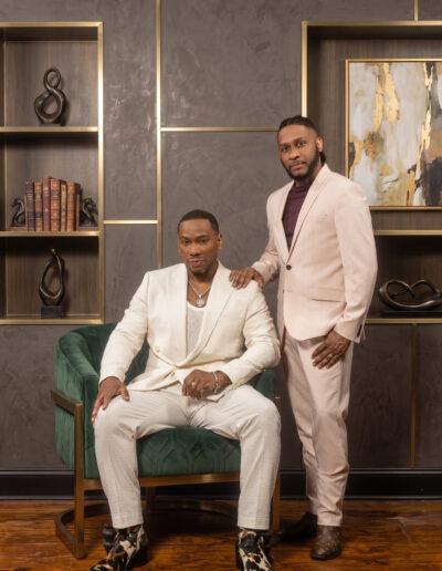 Two men in elegant white and cream formalwear posing in a stylish studio.