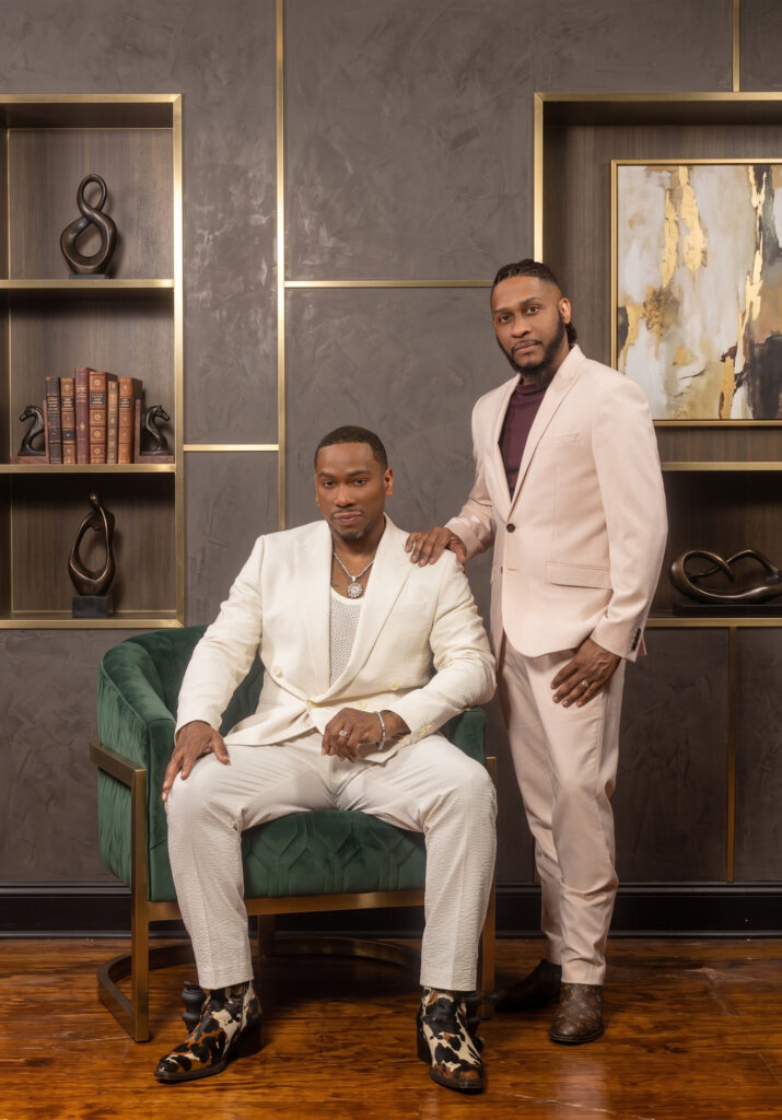Two men in elegant white and cream formalwear posing in a stylish studio.