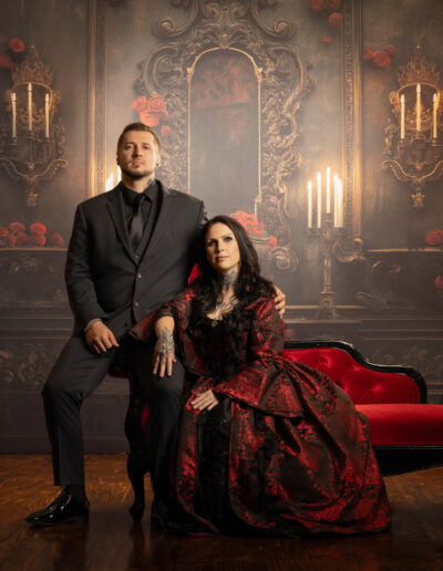 Couple in formal black clothing posed within an ornate dark red room.