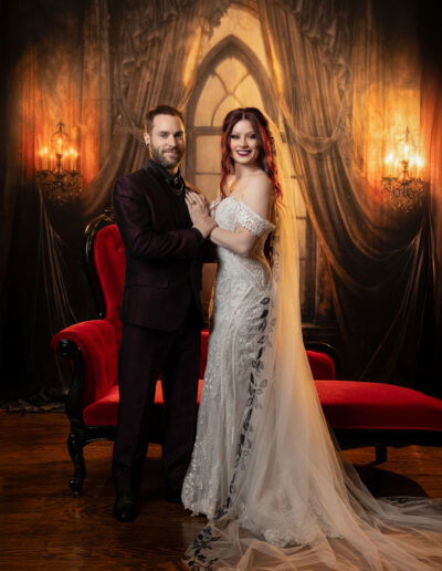 Elegantly dressed couple embracing in a warm candlelit room with rich red accents.