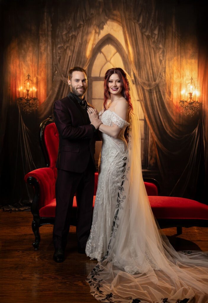 Elegantly dressed couple embracing in a warm candlelit room with rich red accents.