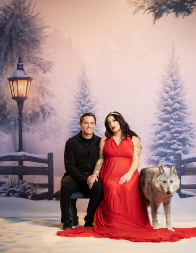 Couple in black and red attire posing together against a snowy winter backdrop.