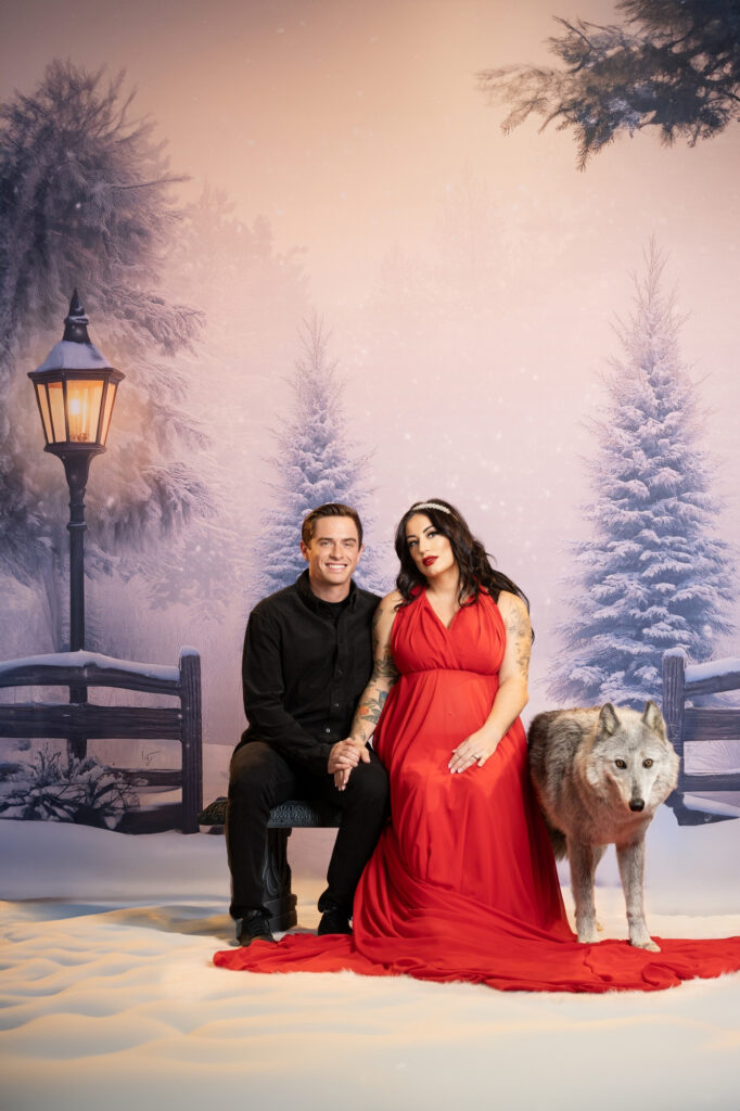 Couple in black and red attire posing together against a snowy winter backdrop.