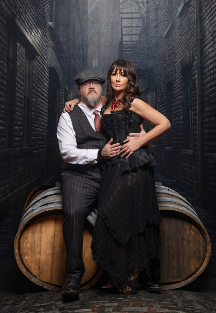 Couple in vintage-inspired clothing embracing against a dark paneled wall.