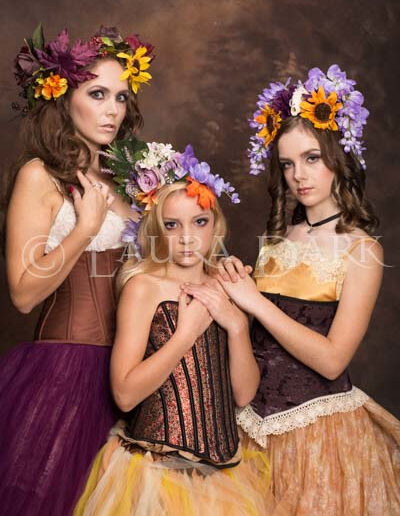 Mother and two daughters wearing colorful floral crowns in a fine-art family portrait.