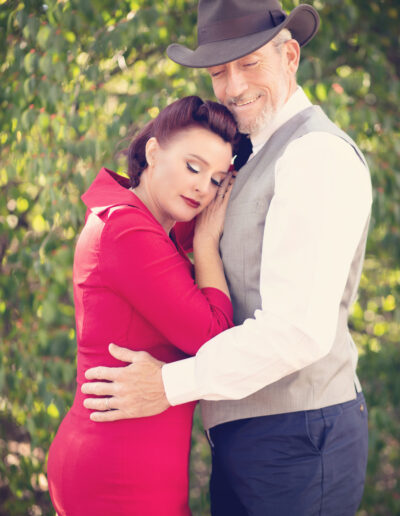 Woman in a red dress resting against her partner during an outdoor couples portrait.