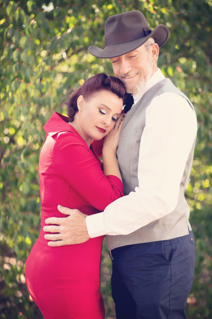 Woman in a red dress resting against her partner during an outdoor couples portrait.