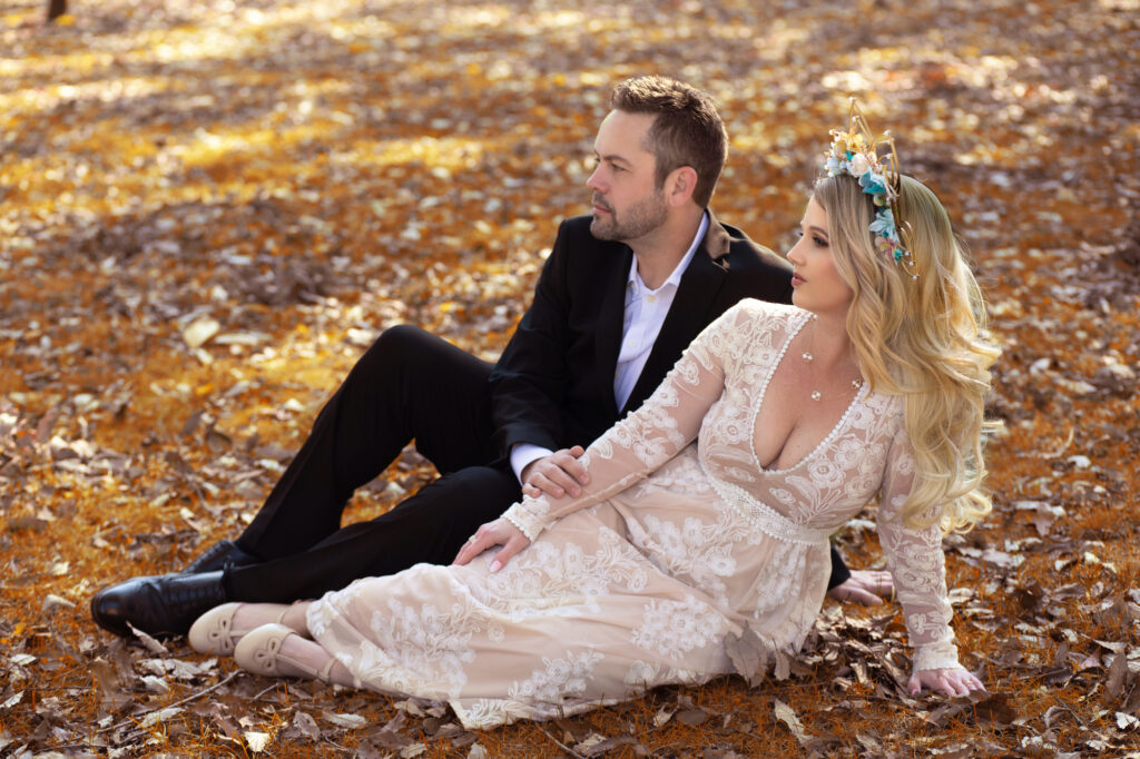 Elegantly dressed couple seated together among golden autumn leaves.