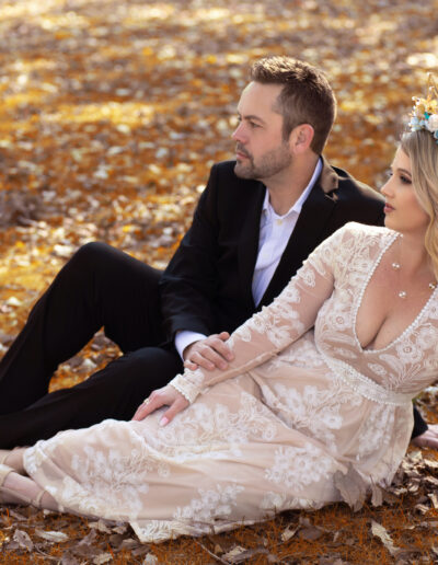 Elegantly dressed couple seated together among golden autumn leaves.