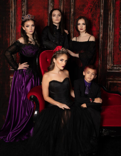 Gothic family in coordinated black and purple clothing posed around a red chair.