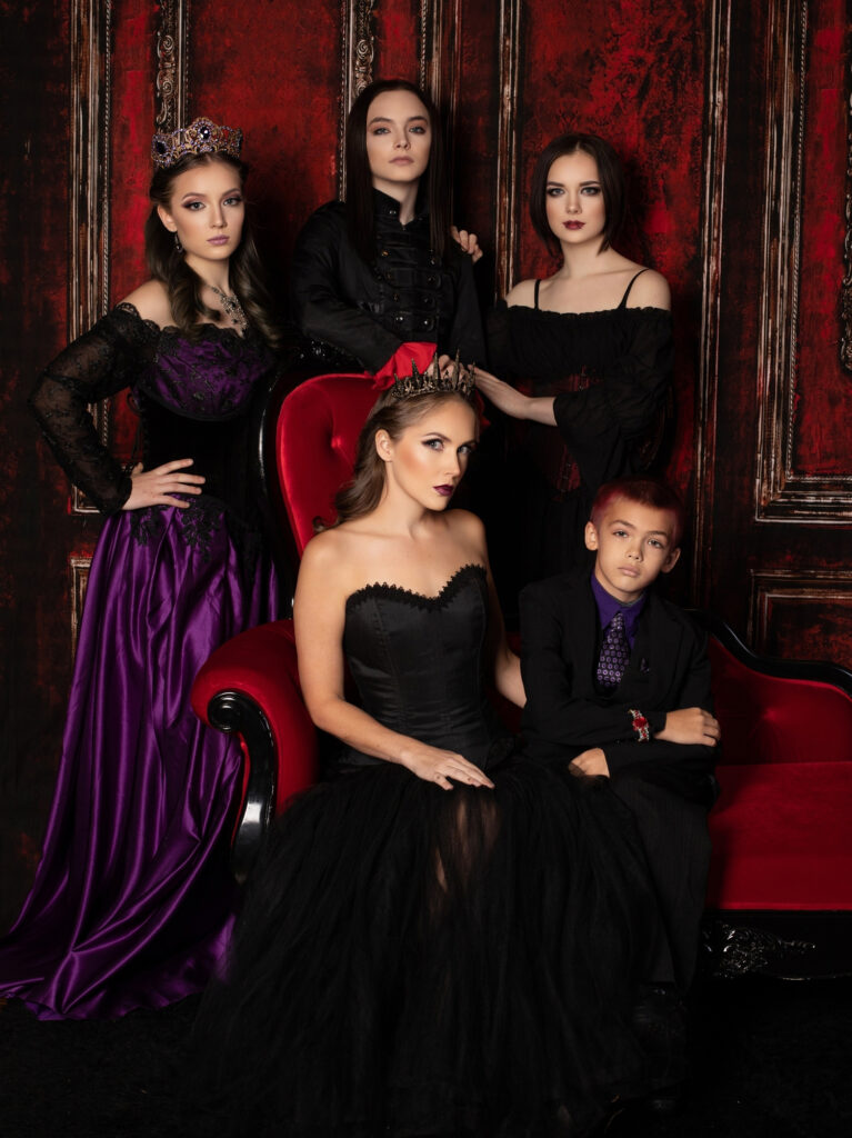 Gothic family in coordinated black and purple clothing posed around a red chair.