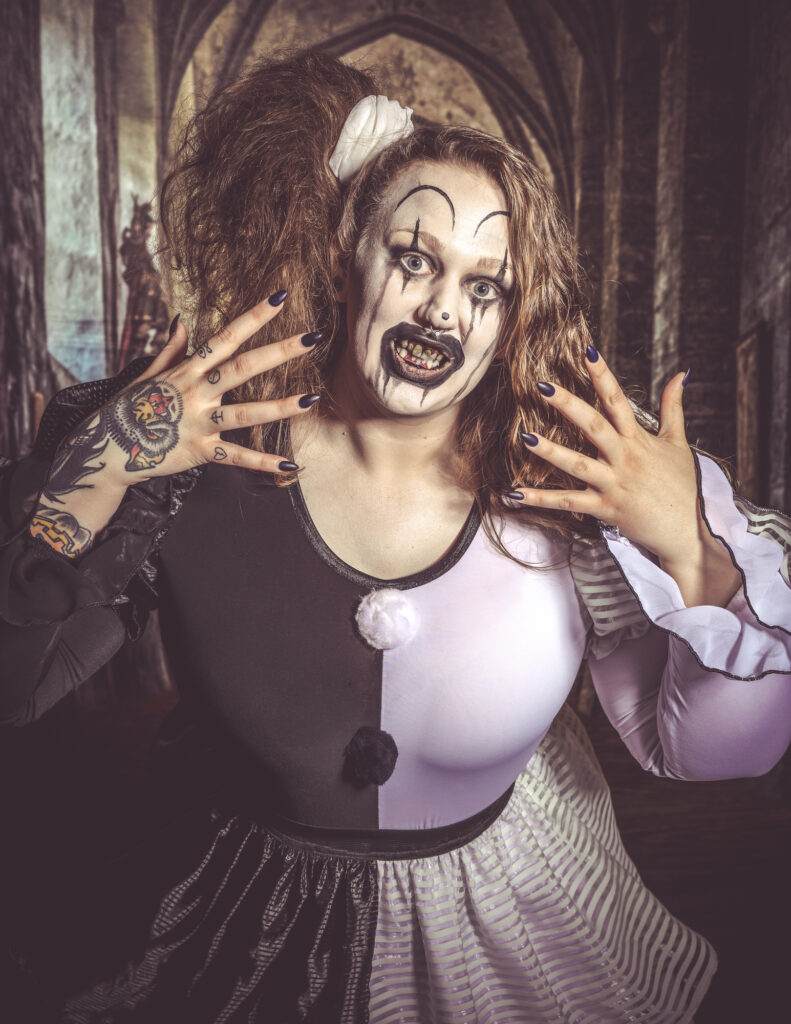 Horror character with theatrical monster makeup and clawed hands framing her face.
