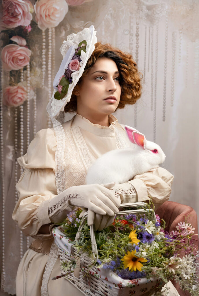 Woman in an ivory Victorian dress and floral bonnet holding a white rabbit and flower basket.