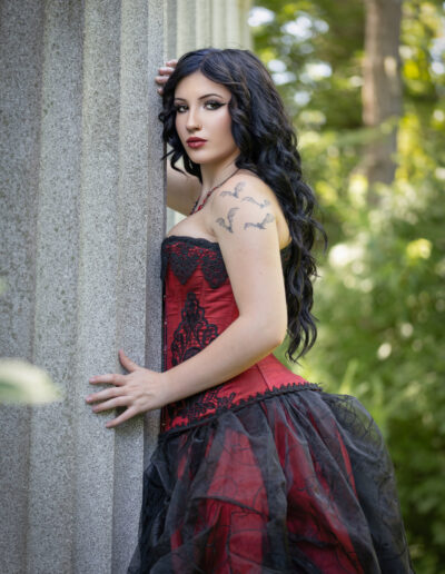 Gothic woman in a red-and-black corset posed beside stone columns