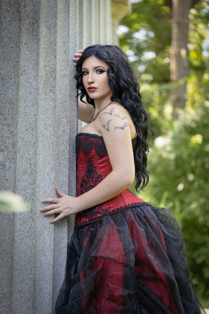 Gothic woman in a red-and-black corset posed beside stone columns
