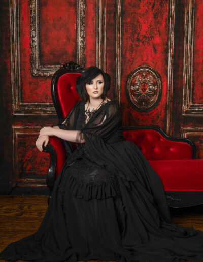 Black-haired gothic woman seated on an ornate red throne