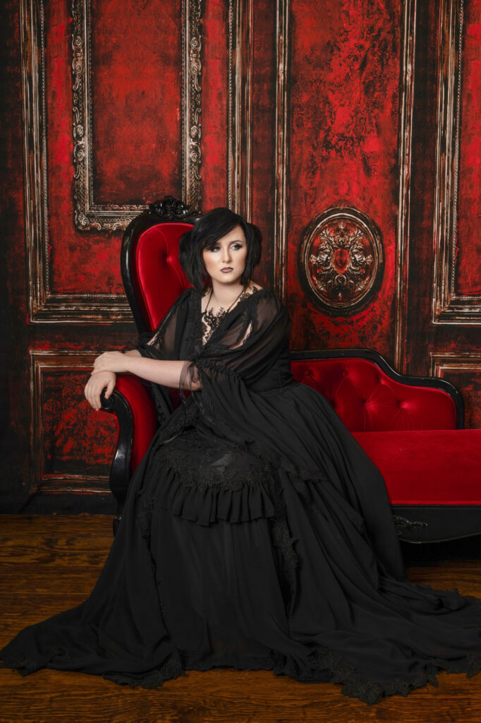 Black-haired gothic woman seated on an ornate red throne