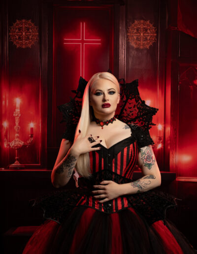 Pale gothic woman in a red-and-black corset against a crimson backdrop