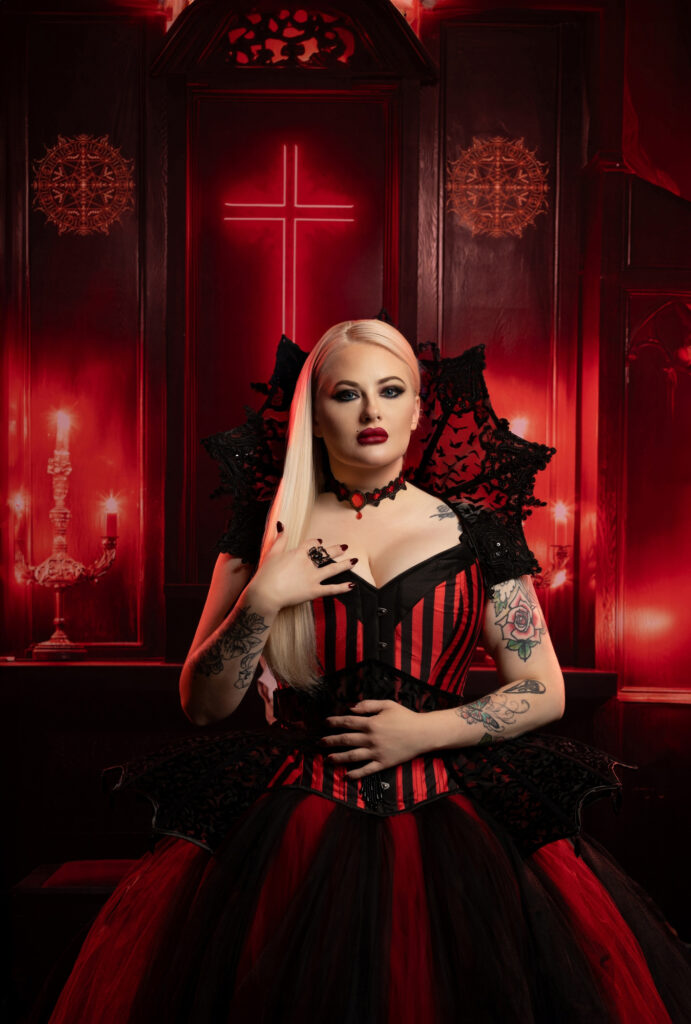 Pale gothic woman in a red-and-black corset against a crimson backdrop