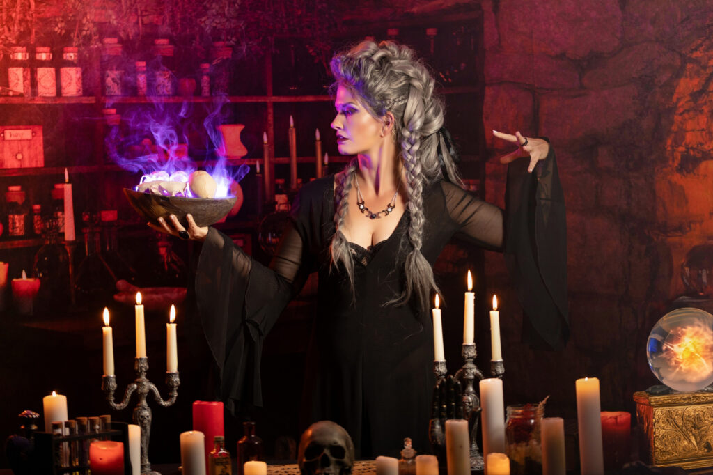 Gothic witch surrounded by candles, potions and glowing purple light