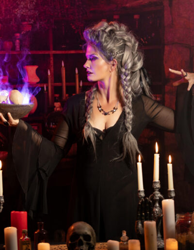 Gothic witch surrounded by candles, potions and glowing purple light