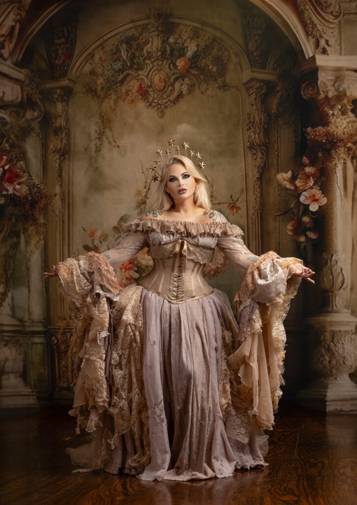 Blonde woman in an ivory corseted period gown with dramatic lace sleeves and a star halo.