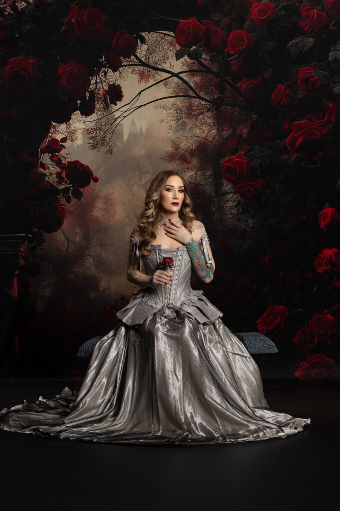 Dark romantic woman in a silver gown surrounded by black and red flowers
