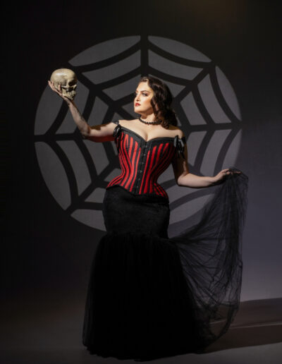 Gothic woman in a red-and-black corset posed against a spiderweb backdrop