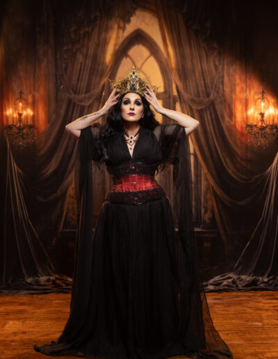Haunted gothic woman in black inside a dramatic curtained room