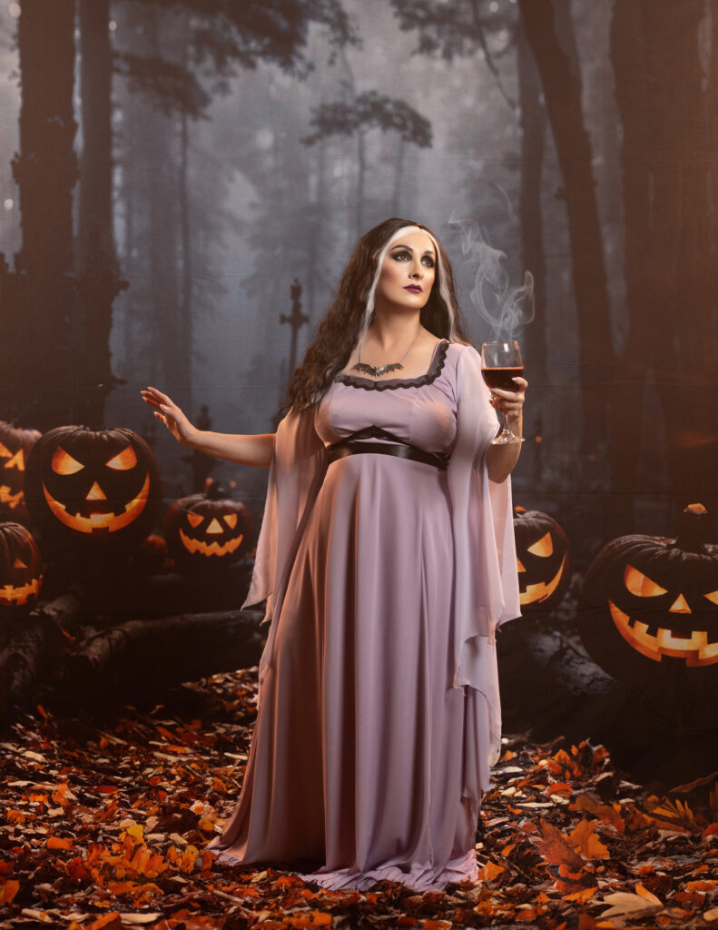 Woman in a flowing mauve gown standing among glowing jack-o’-lanterns.