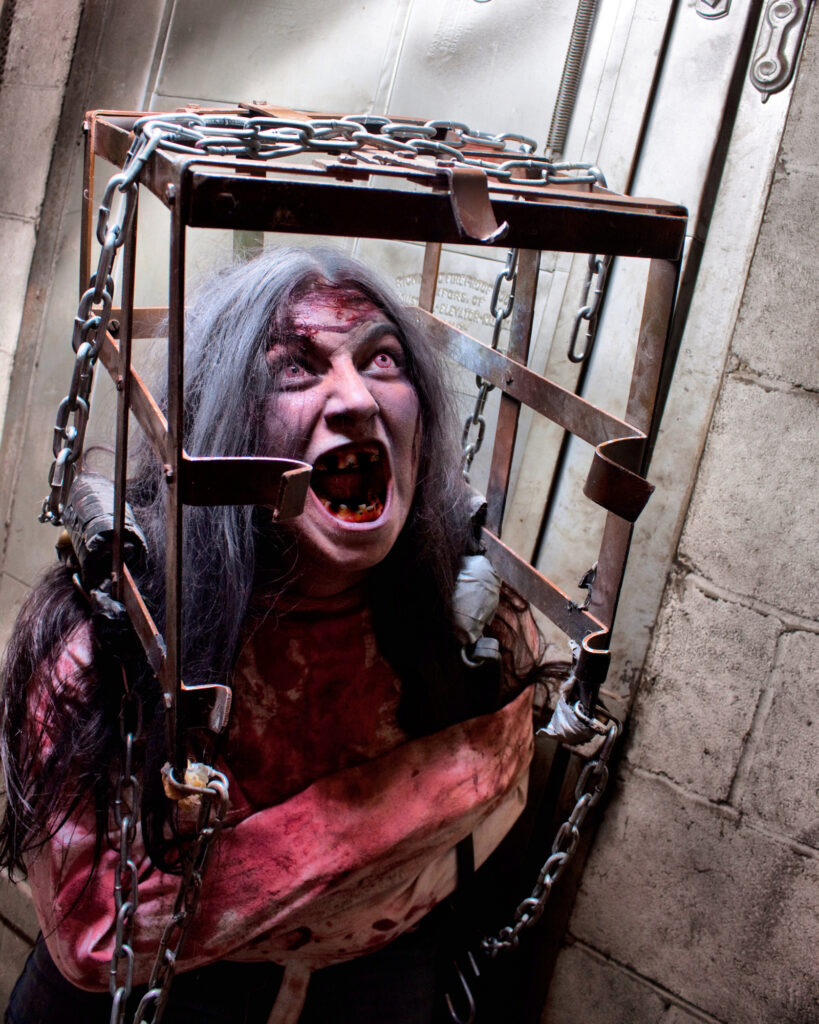 Bloodied horror character screaming through the bars of a rusted metal cage.