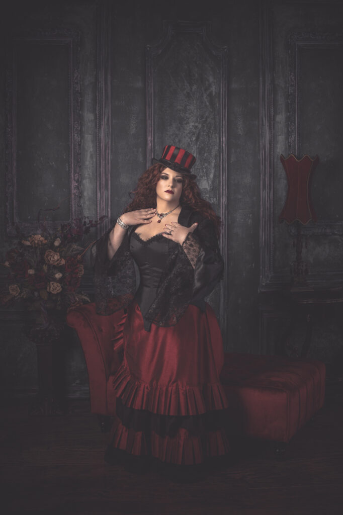 Woman in a red and black steampunk gown and striped top hat in a smoky Victorian parlor.