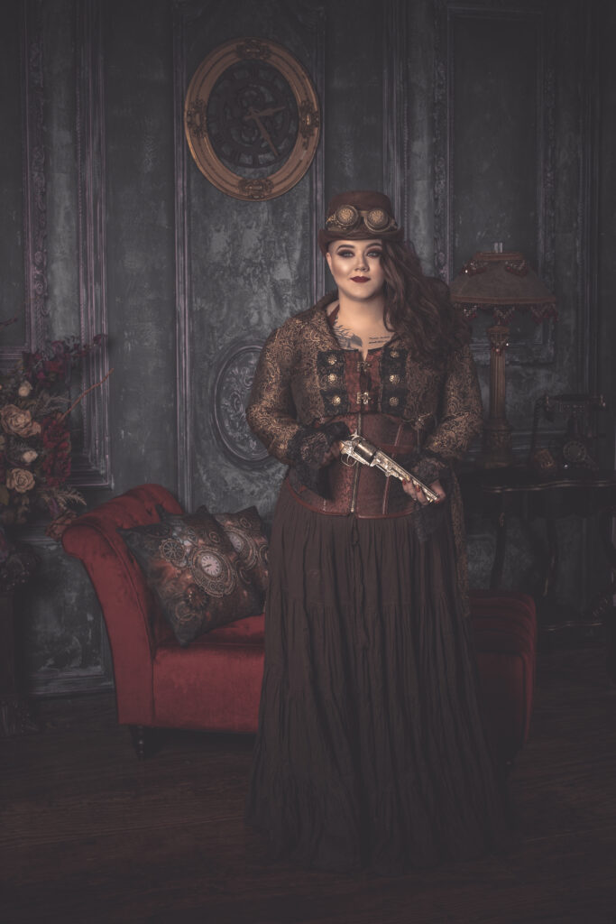Woman in a brown steampunk outfit and goggles posing in an ornate blue room.