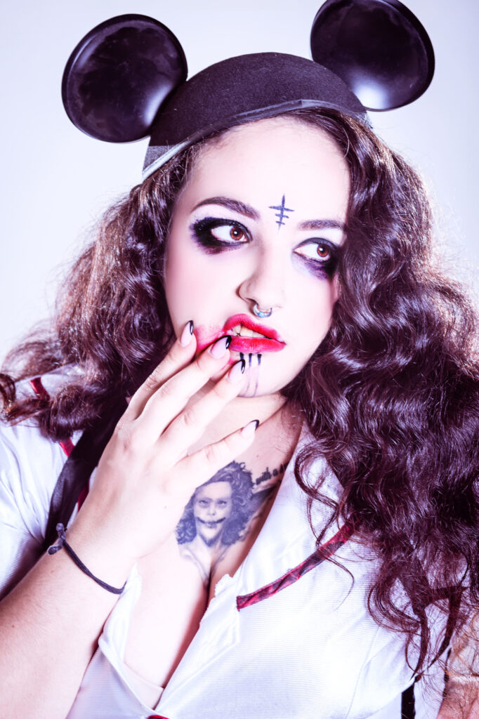 Pale gothic character with dark eye makeup, painted symbols and blood-red fingertips.